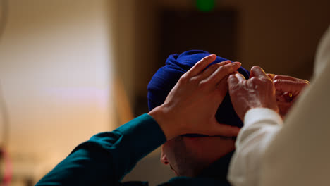 Close-Up-Studio-Shot-Of-Senior-Sikh-Man-Helping-Younger-Sikh-Man-To-Tie-Fabric-For-Turban-Against-Plain-Background-Shot-In-Real-Time